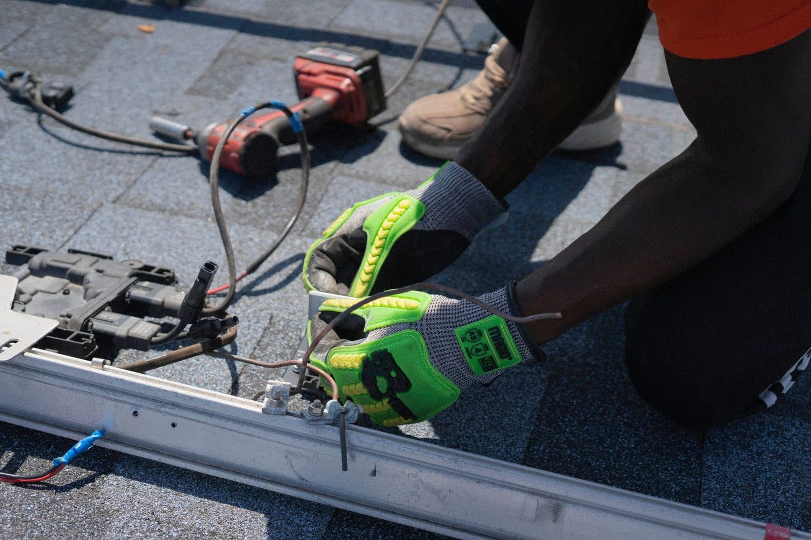 Solar installer in work gloves connecting panel wiring to mounting rail on a shingle roof