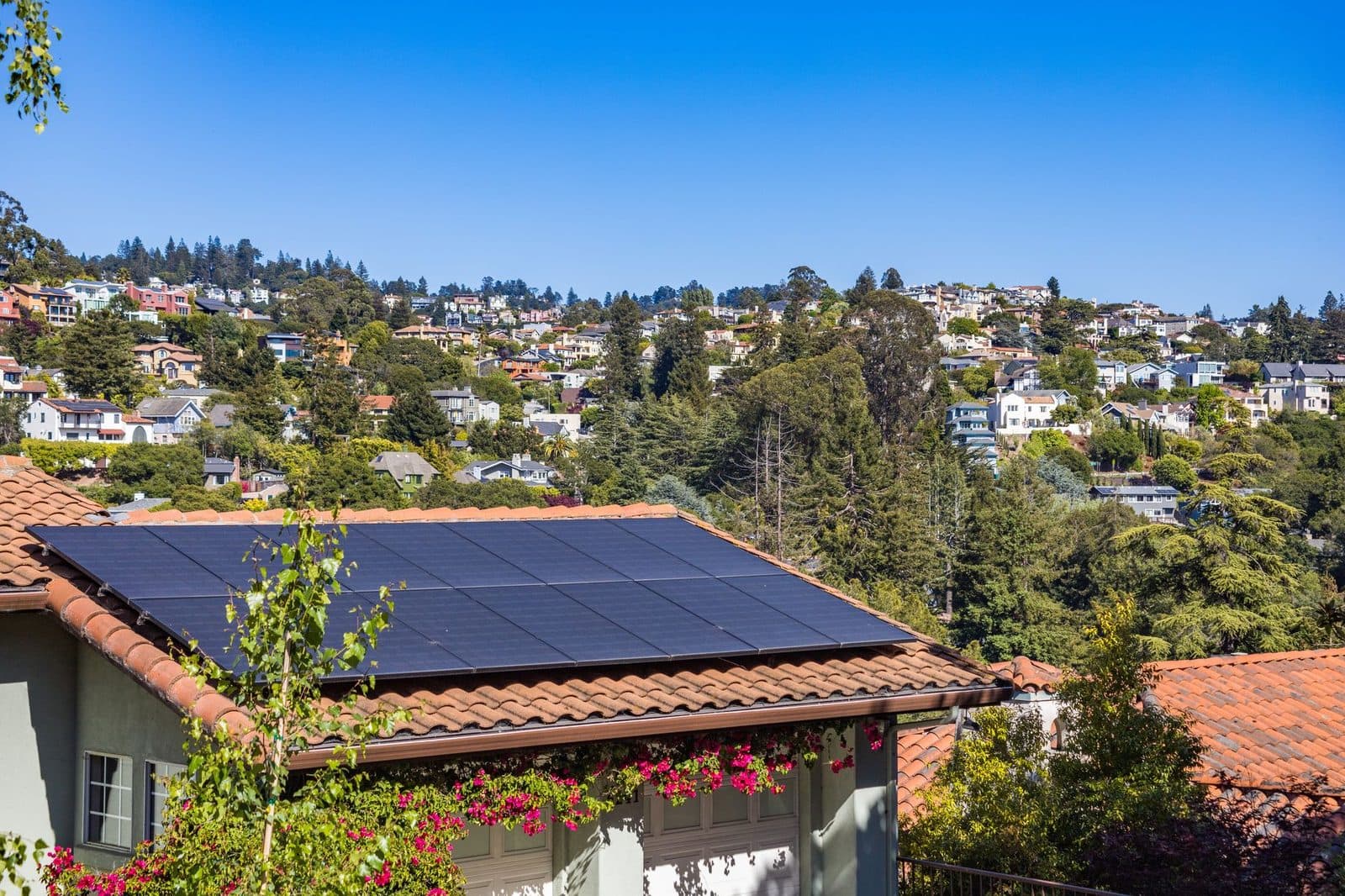 Rooftop solar array on a tile-roofed home overlooking a hillside neighborhood