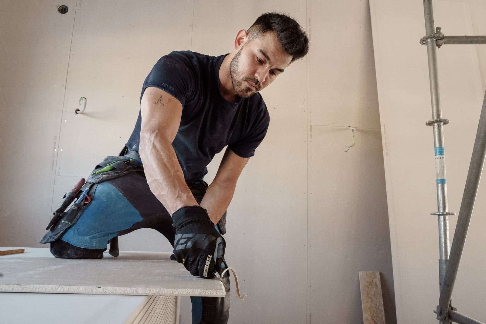 Tradesman in a tool belt cutting a sheet of plasterboard during interior repair work