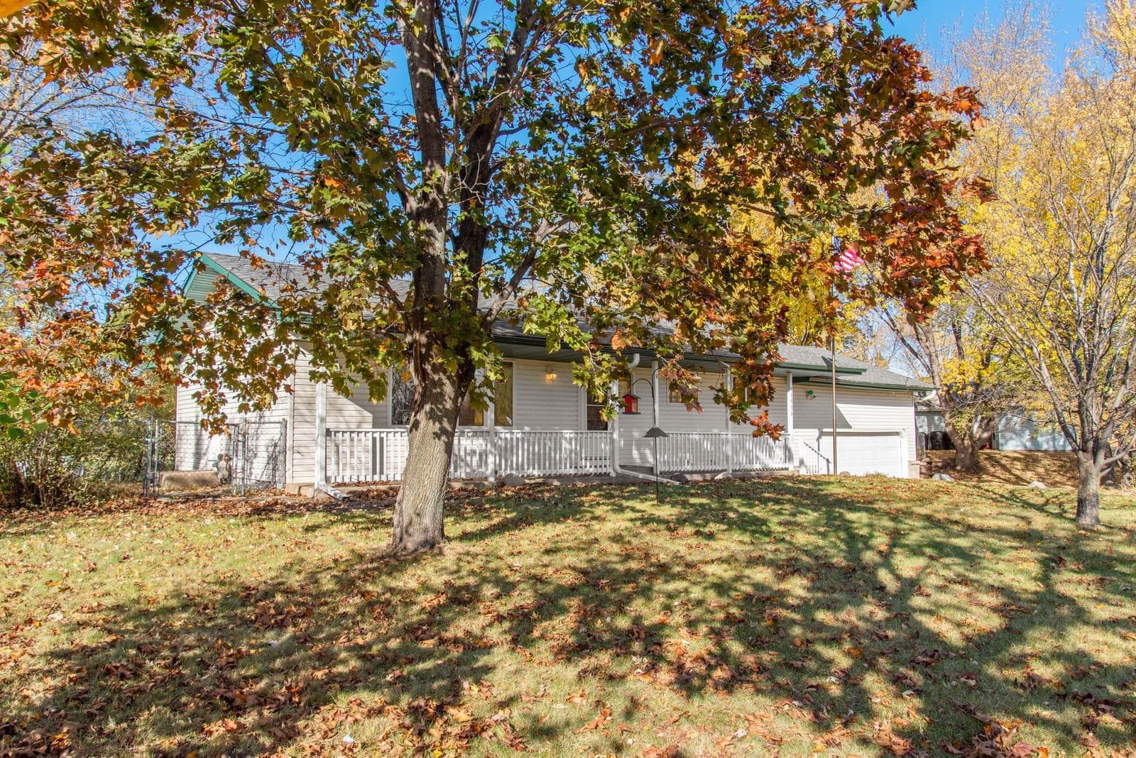 A single-story American home with a white porch railing and attached garage, fallen autumn leaves across the front lawn