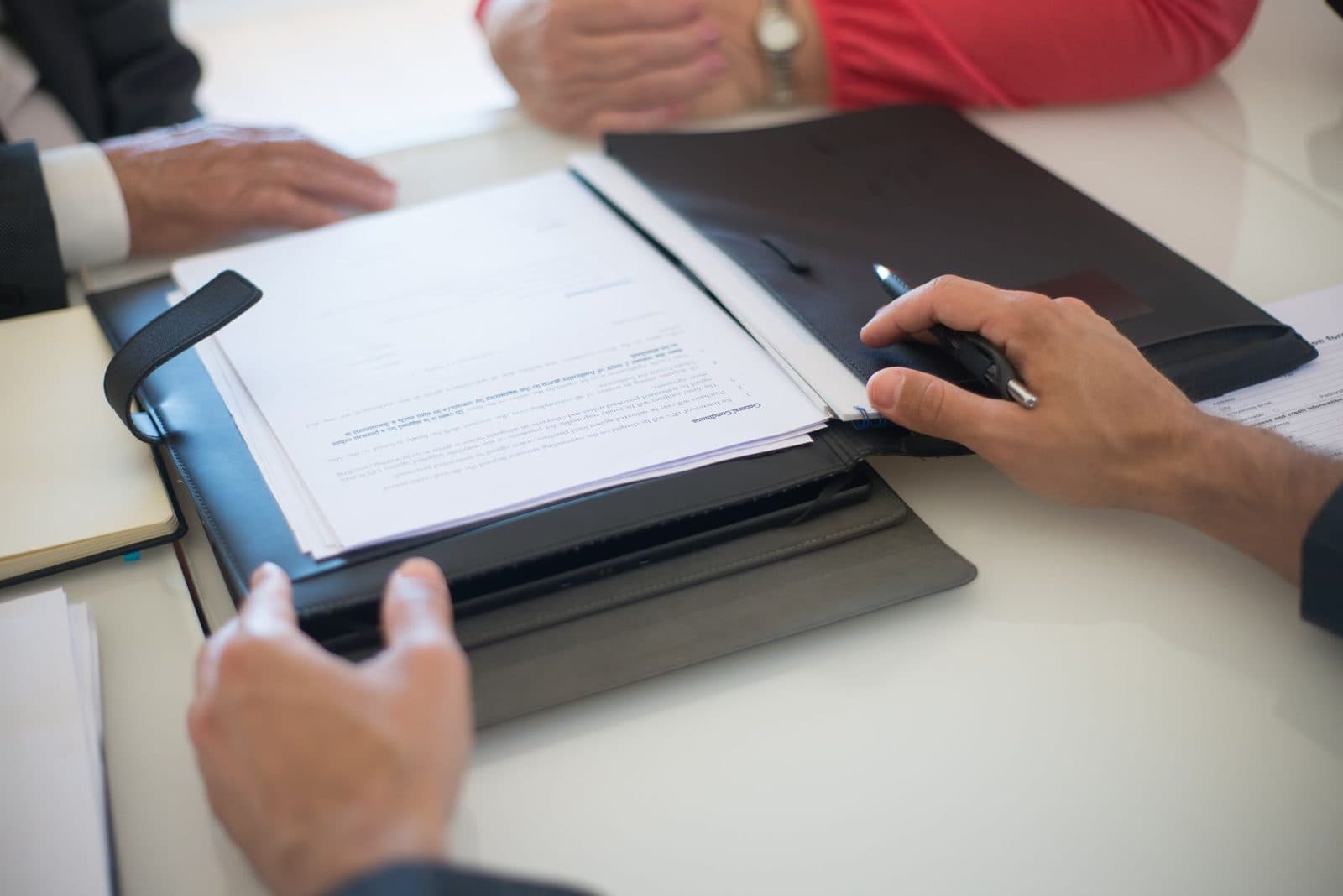 Two people seated at a table reviewing a printed contract in a folder, one holding a pen ready to sign